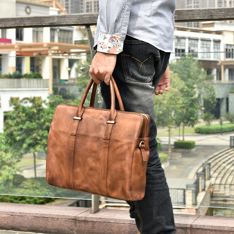 Vintage cowhide leather handbag displayed with a 14-inch laptop and daily accessories for size reference.